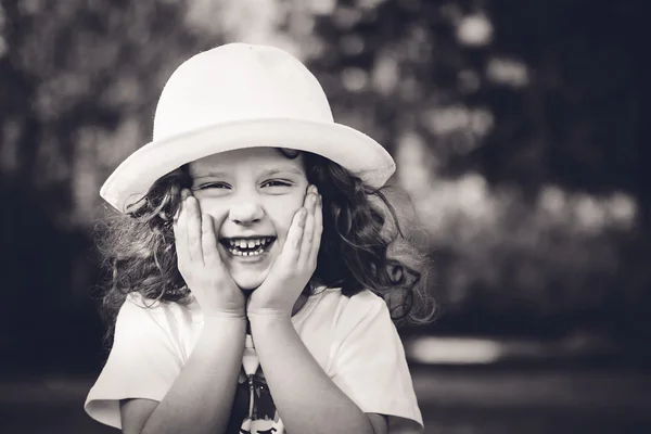 Black and white portrait of curly girl in a white hat.