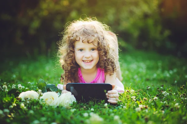 Little girl sitting on grass and hold white flowers and tablet pc