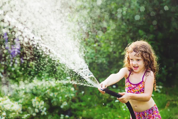 Happy curly girl under water splashes in the summer garden.