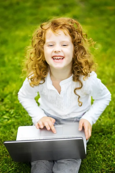 Happy surprised child with laptop sitting on the grass.