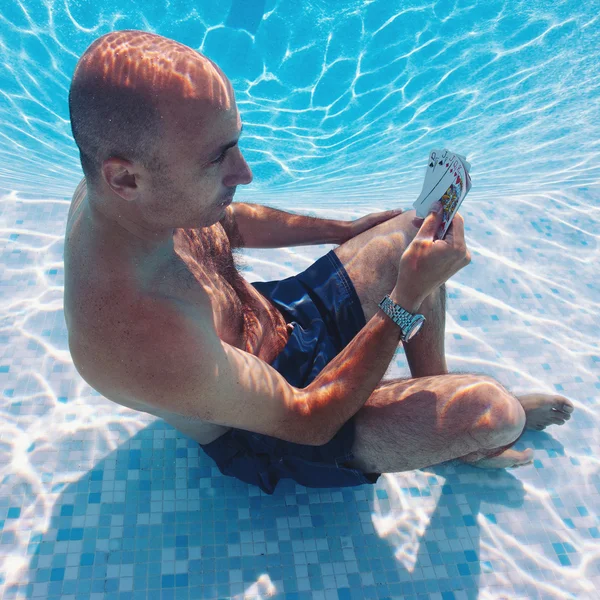 Underwater portrait of man playing poker inside a swimming pool.