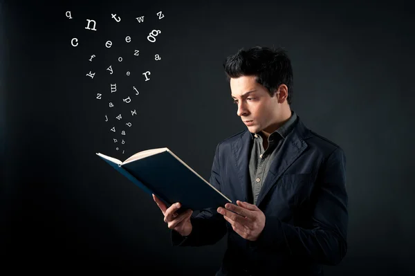 Young man reading book with letters coming out against dark background