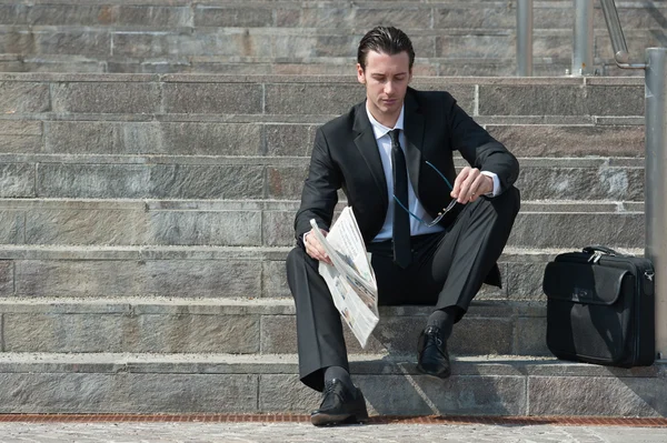 Young business man with newspaper sitting on the stairs