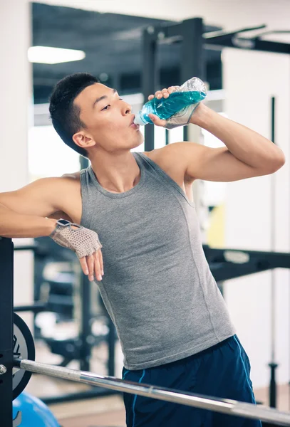 Young asian man having a rest drinking a beverage in the gym