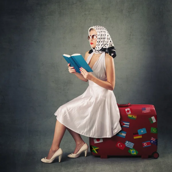 Retro woman with sunglasses and suitcase reading book portrait against grey background