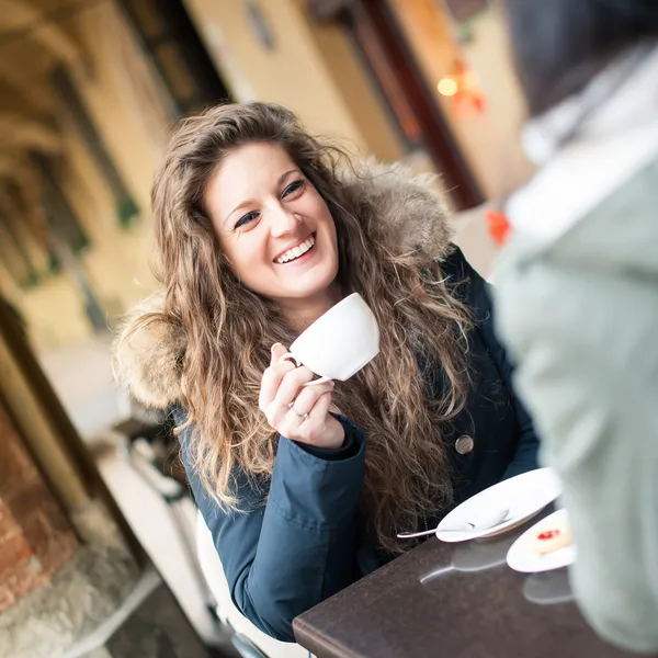 Young woman drinking coffee with friend in a cafe outdoors. Shallow depth of field.