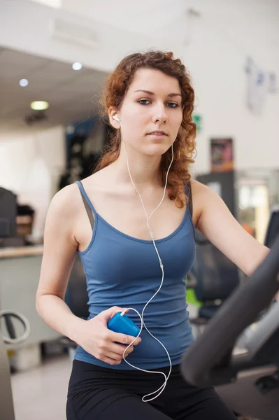 Young woman training in the gym with bike while listening to mus