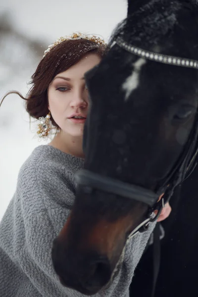 Lovely and beautiful girl of the European appearance brunette with brown horse in winter nature with accessories. Fashion and beauty. Animal and natural.