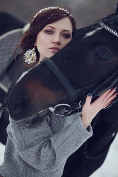 Lovely and beautiful girl of the European appearance brunette with brown horse in winter nature with accessories. Fashion and beauty. Animal and natural.