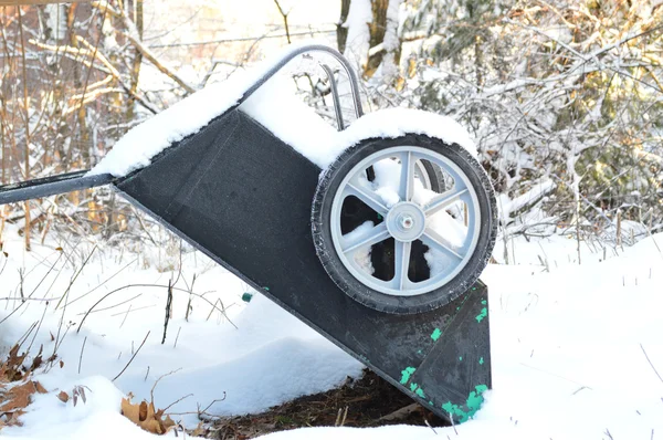 Old snow covered wheelbarrow leaning upside down in the backyard