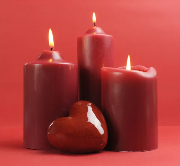 Three romantic red lit candles against a red background.