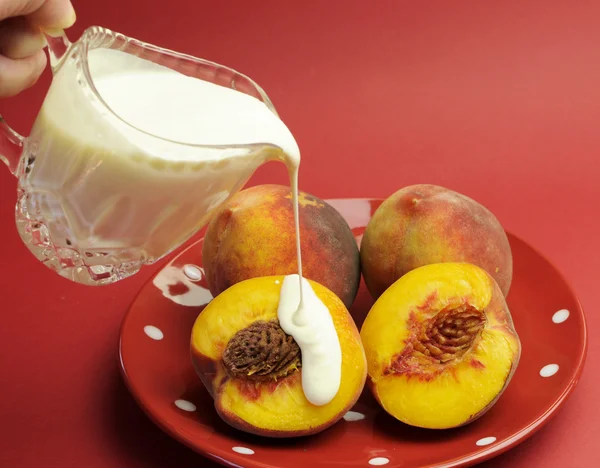 Pouring cream over delicious summer peaches fruit for 'peaches and cream' concept.