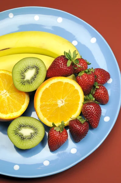 Platter of fruit - bananas, orange, kiwi fruit and strawberries - on blue polka dot platter for healthy diet and fitness. vertical.