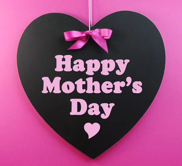 Heart shape blackboard with pink ribbon on pink background with Happy Mothers Day message.