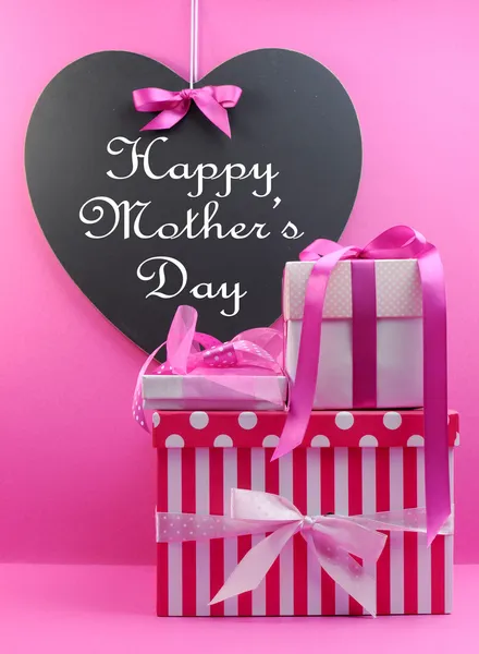 Stack of beautiful pink stripe and polka dot present gifts with heart shape blackboard with Happy Mothers Day message.