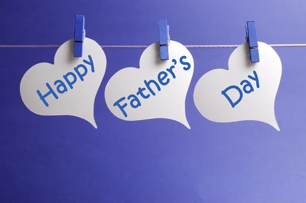 Happy Fathers Day message written on white heart shape tags hanging from blue pegs on a line against a blue background.