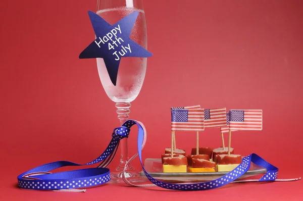 USA Happy Fourth 4th of July party table setting with flags, ribbons, polka dots, and stars and stripes champagne glass and cocktail food.
