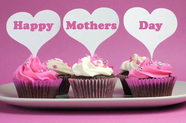 Happy Mother's Day message across white heart toppers on pink and white decorated red velvet cupcakes on pink background.