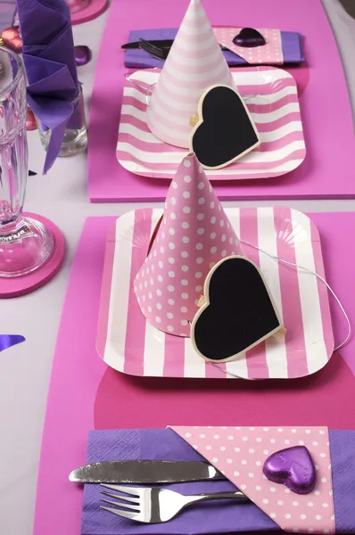 Pink and purple theme party table setting decorations. Vertical with party hats and pink strip plates.