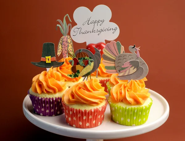 Happy Thanksgiving decorated cupcakes with turkey, pilgrim hat and corn toppers on cake stand against a brown background, with Happy Thanksgiving message.