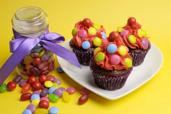 Colorful red blue yellow and red candy covered cupcakes with candy jar