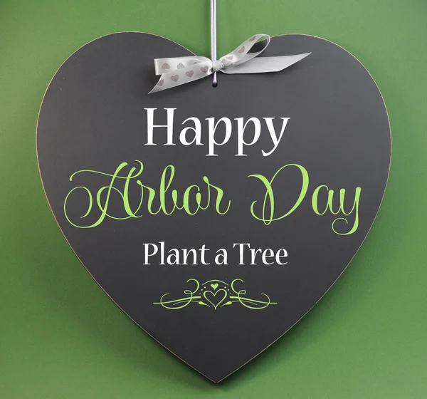 Happy Arbor Day, Plant a Tree, greeting message sign on heart shaped blackboard against a green background.