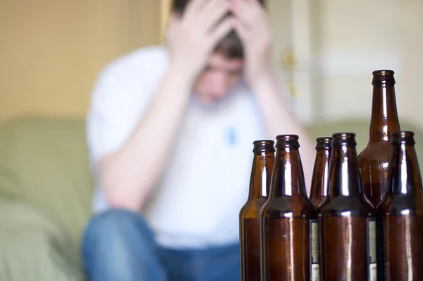 Man holds head with group of empty beer bottles