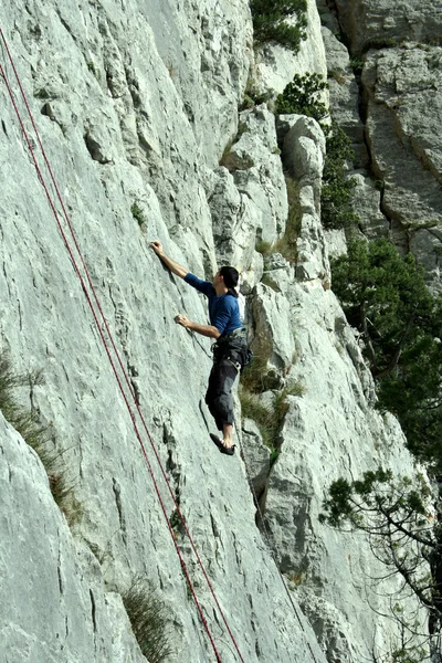 Young man climbing vertical wall with valley view on the background