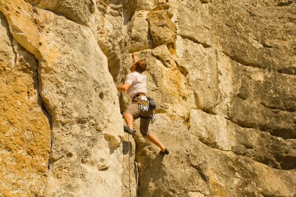 Young man climbing vertical wall with valley view on the background