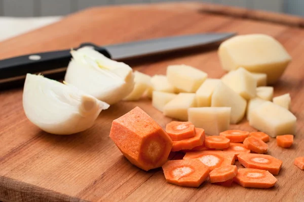 Onion, carrots and potatoes on a wooden chopping board