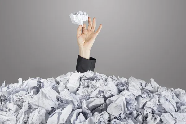 Person under pile of documents with hand holding a crumpled paper