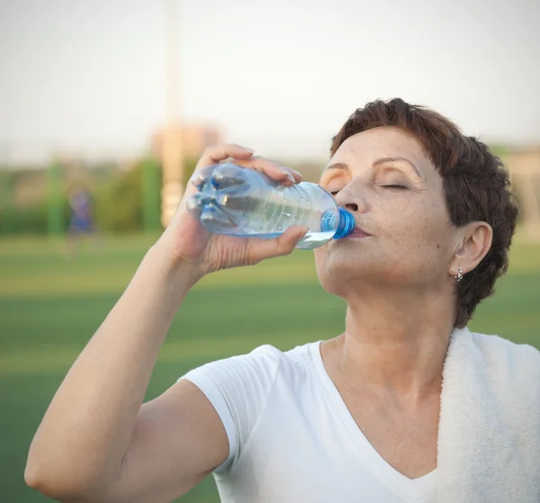 Attractive woman 50 years old, drinking water after fitness