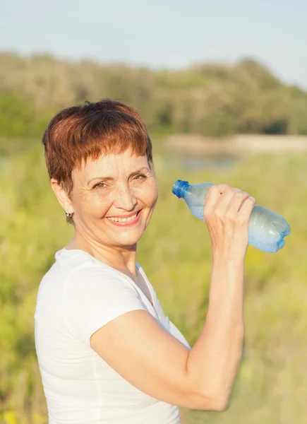 Sports woman  50 years with a  bottle of water, outdoors