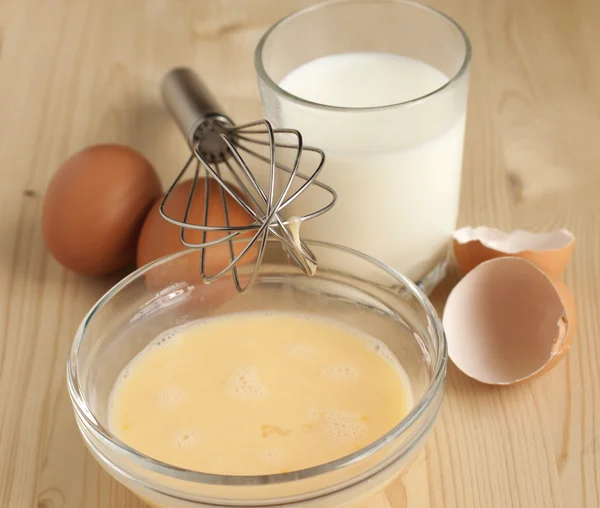 Beat eggs with milk in a glass bowl , eggs on a wooden table.