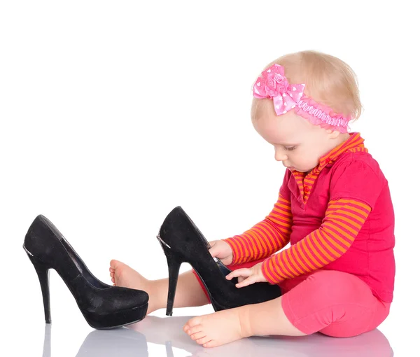 Cute little baby girl trying on her mother's shoes on white back