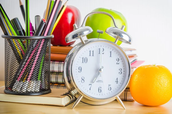 Note books, clock, pencils, apples on the table
