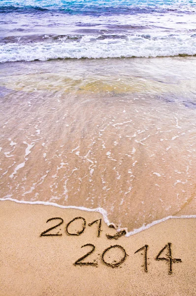 New Year 2014 is coming concept - inscription 2013 and 2014 on a beach sand, the wave is covering 2013