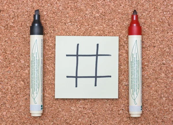 Blank tic tac toe game on sticky note with red and black markers