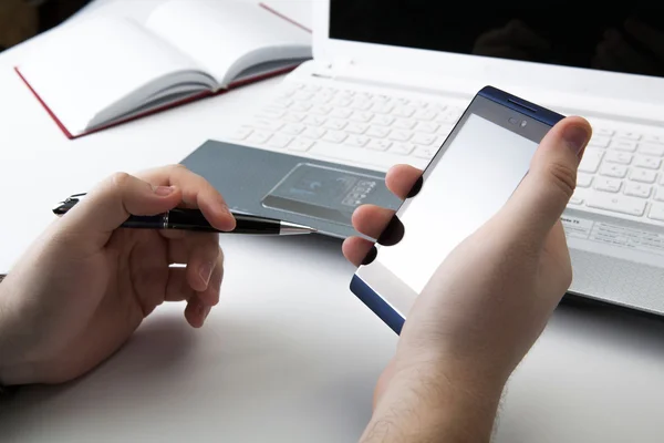 Human fingers near the notebook keyboard and smartphone