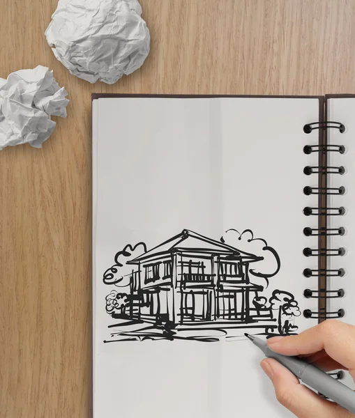 Hand drawing house on wrinkled paper with wooden table as concep