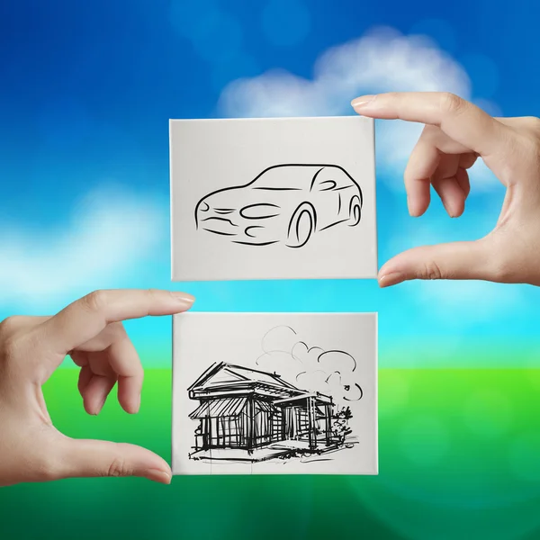 Hand holding hand drawn house and car on canvas board on nature