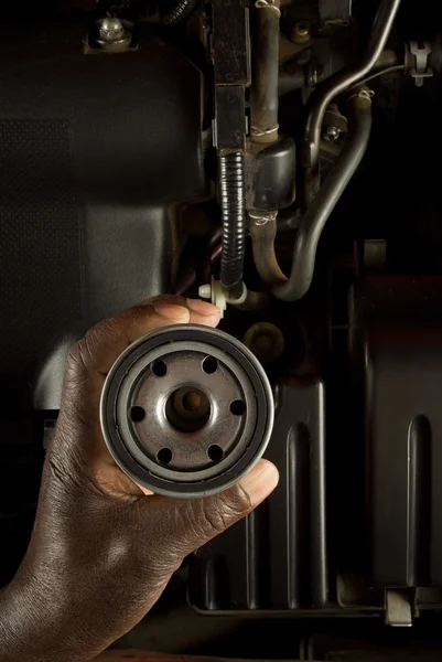 South African or American hand holding oil filter with modern car engine background
