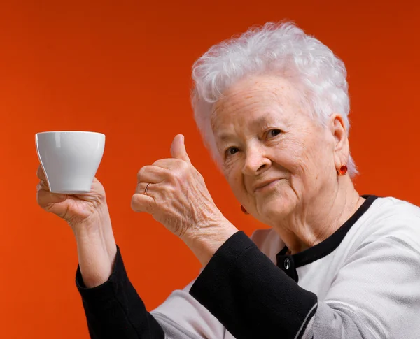 Old woman in glasses enjoying coffee or tea cup