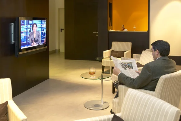 Man reading newspaper and watching TV news at Hotel