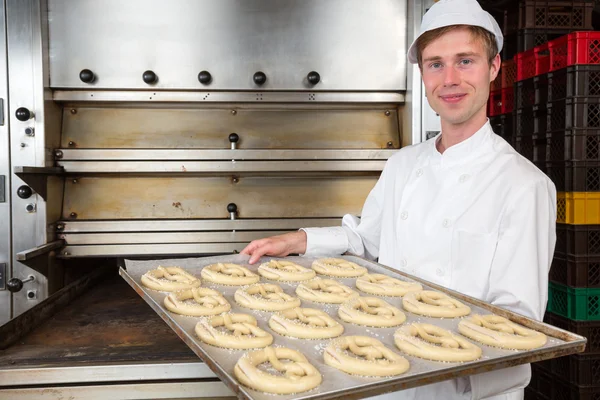 Baker in bakery with baking plate full of pretzels