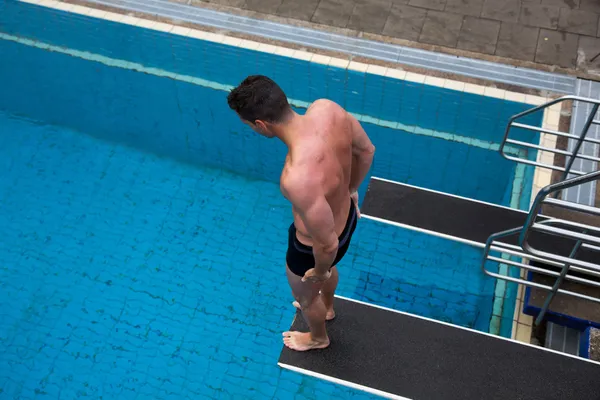 Man standing on diving board at public swimming pool