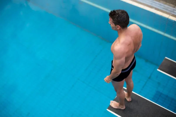 Man standing on diving board at public swimming pool