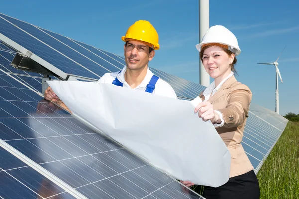 Photovoltaic engineers with construction plan at solar panels