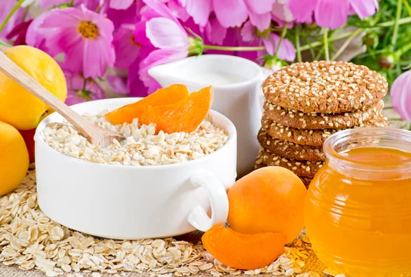 Oatmeal with apricot, milk jug, cookies, honey and flowers