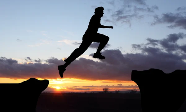Silhouette of hiking man jumping over the mountains at sunset